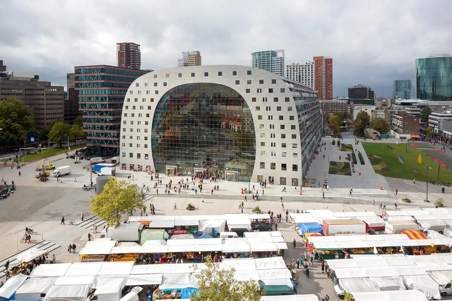 Der er to typer torvehandel: I forgrunden ses et traditionelt marked, hvor varer af forskellig art sælges fra teltoverdækkede vogne. I baggrunden Rotterdams nye markedsplads med lejligheder indrettet i bygningens sider og loft.