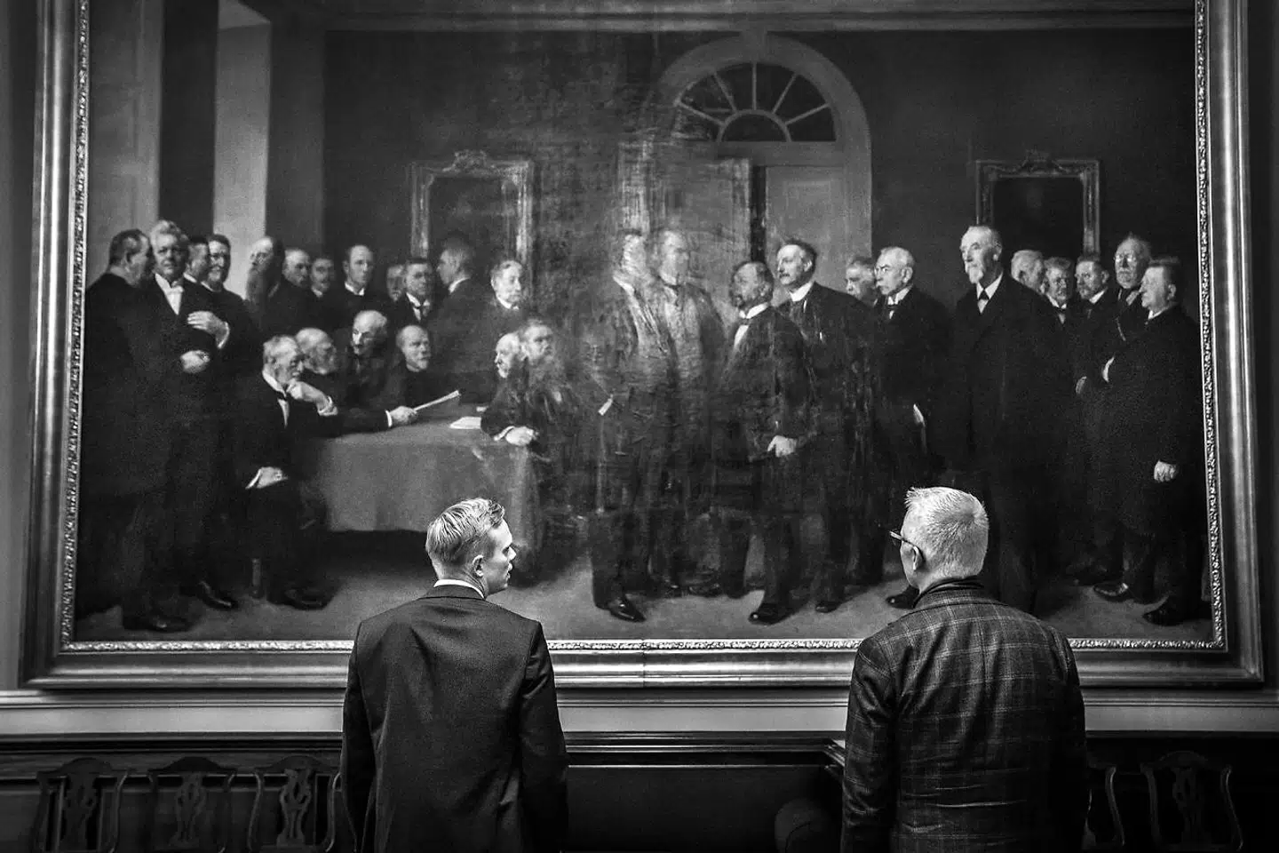 Med mål på mere end fem gange tre meter tårner en række rigsdagsmedlemmer sig op i en diskussion af det endelige indhold af den Grundlovsændring, der i 1915 gav kvinder og tjenestefolk stemmeret. Maleriet er af Herman Vedel og fylder den ene endevæg i Samtaleværelset på Christiansborg. Foran det kan selv store erhvervsfolk som Grundfos' Mads Nipper (t.h.) og Boston Consulting Groups Anders Fæste blive ydmyge.