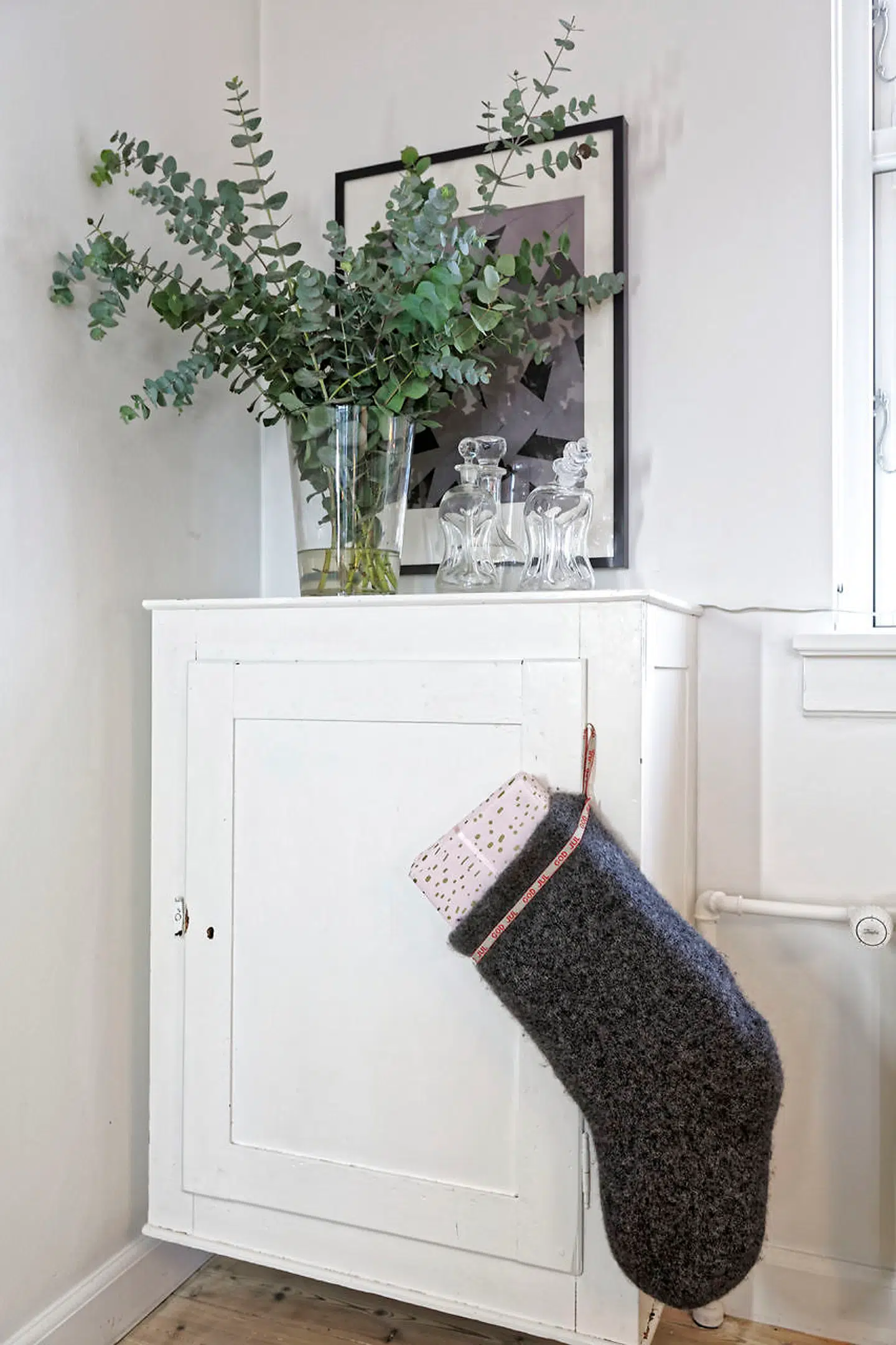 Det hvide skab rummer spil, som bruges flittigt i julen. I vasen står Eukalyptusgrene, mens filtsokken er syet af en veninde og rummer adventsgaver.