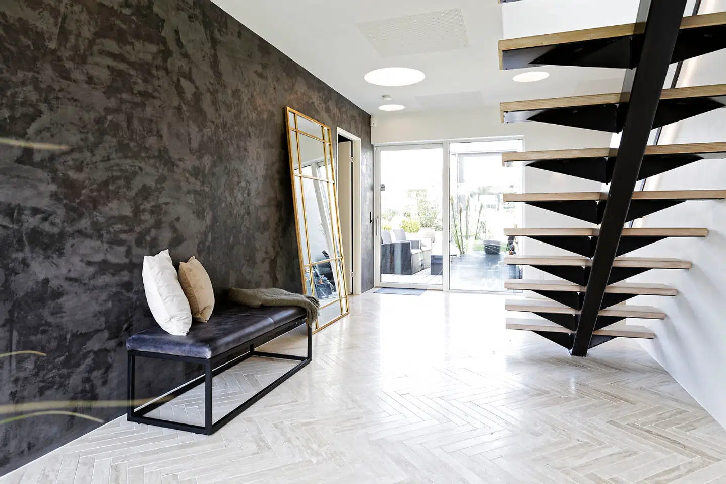 Fra entreen med sildebenslagt travertinmarmor fører en trappe med lysdioder i gelænderet til overetagen. Væggen er bemalet med Kabe kalkspartel.