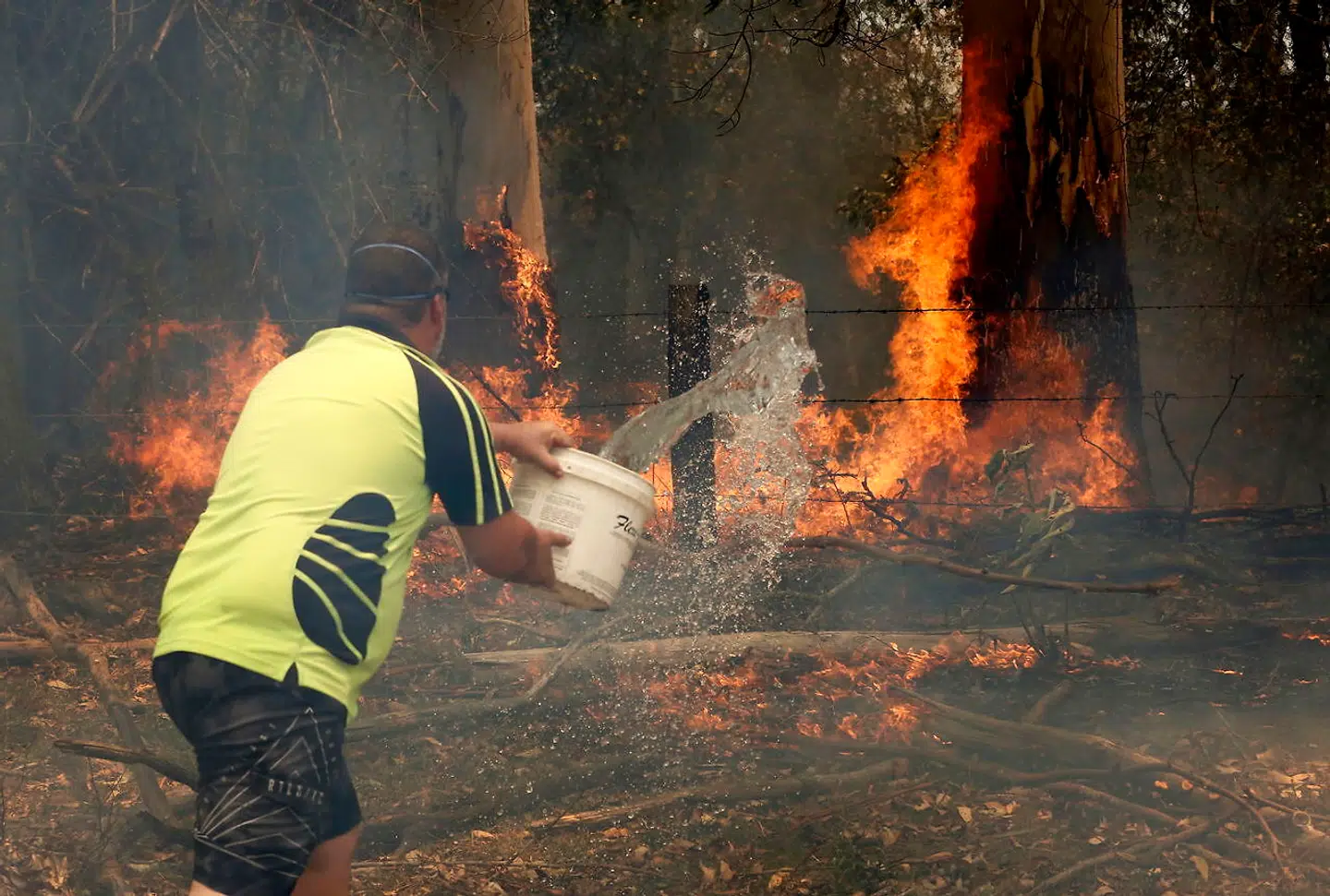 En mand kaster vand på en skovbrand i Koorainghat i New South Wales. Brandene begyndte for alvor at sprede sig fredag i New South Wales, og nu er de katastrofalt farlige.