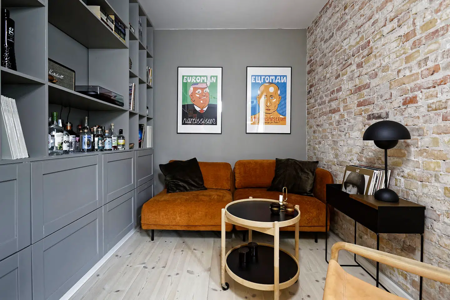 Hvor der før var soveværelse, er der nu stue i forlængelse af køkkenet. Ydervæggens puds er fjernet, mens reolen med skabe er udført af IKEA, Emilie Bjørnskov og hendes far. Sofaen er fra The Sofa Company og de nummererede litografier er kreeret af kunstneren HuskMitNavn.