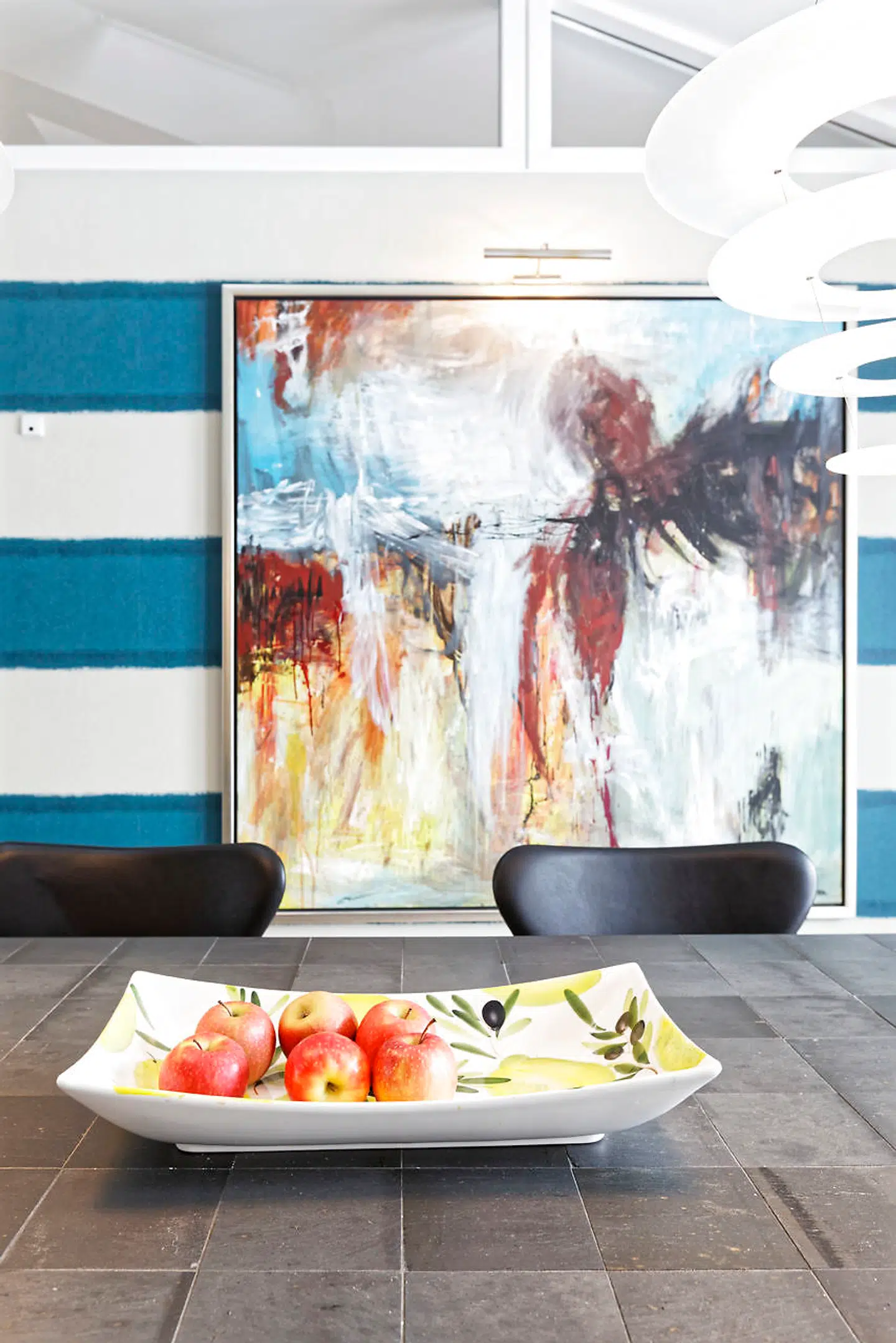 Væggene ved spisepladsen i køkken-alrummet er beklædt med tapet fra Harlequin i brede, vandrette hvide og blå striber. Bordet fra Rübner er beklædt med genbrugsskifer fra taget af Odd Fellow Palæet, da det blev renoveret. Maleriet er af den lokale Lejre-kunstnergruppe Abstra.