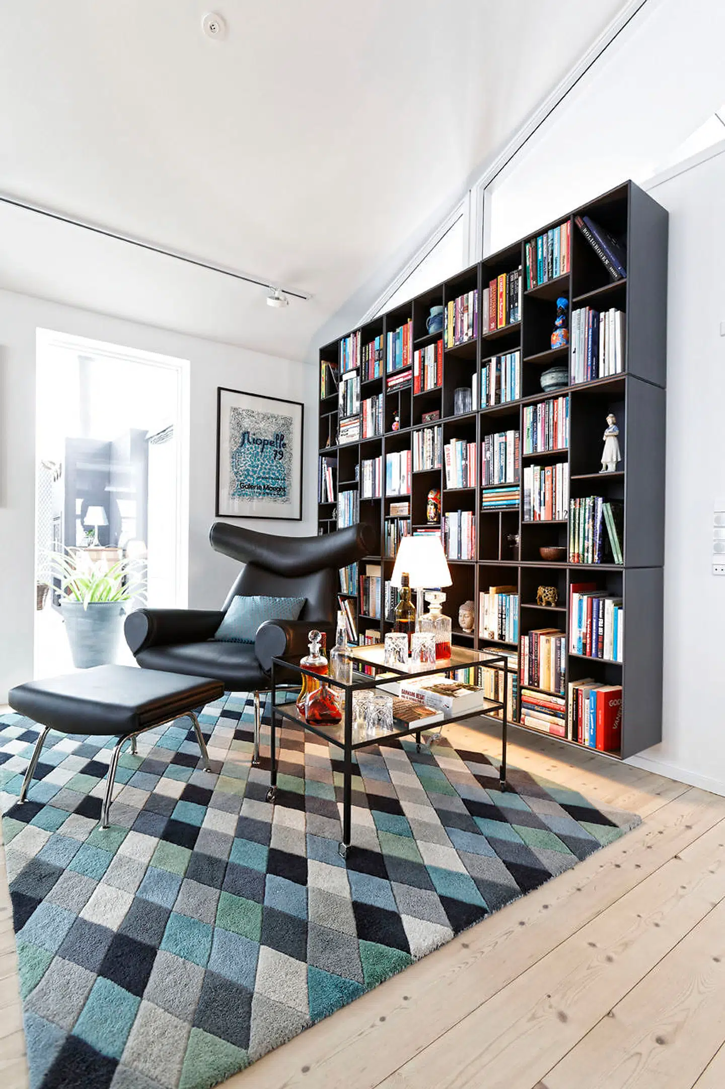 I stuen med åbent til kip er blågrå kulører og mørk Montana reol med læseplads i Hans J. Wegners Ox-chair på tæppet fra Ilva. Sofaen er fra Bolia, mens pufs og puder er fra Boelskifte Interiør & Design.