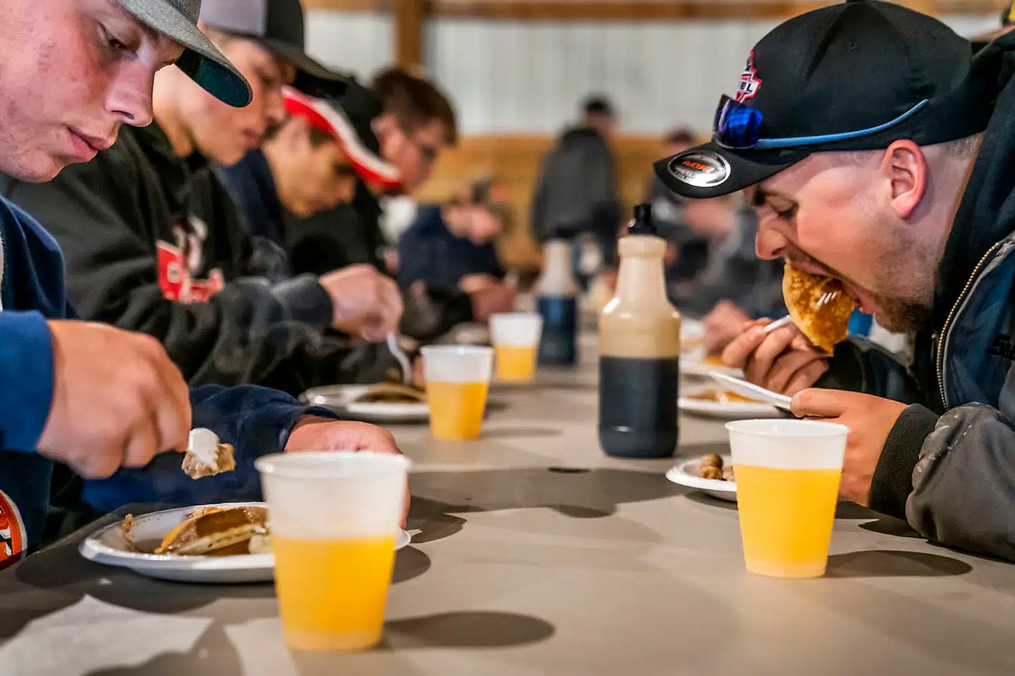 Ved bordene i laden går snakken om Trumps handelskrig, mens der spises pandekager med et ordentligt lag sirup.