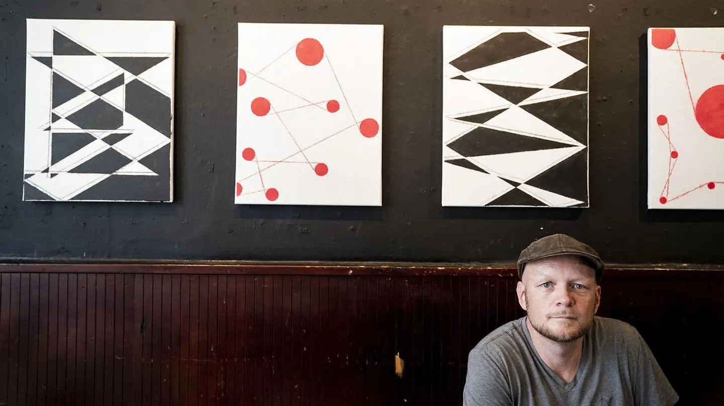 Jonas Hvid Søndergaard foran nogle af de malerier, han for tiden udstiller på Byens Kro.