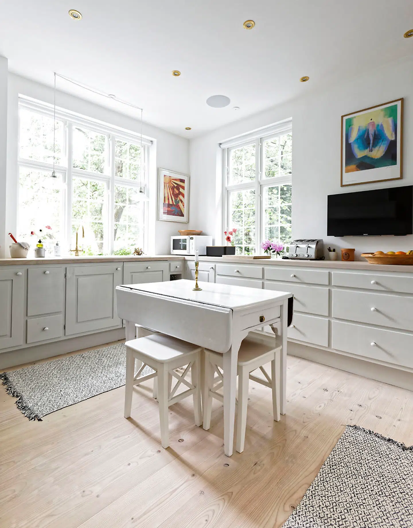 Forrammekøkkenet fra Dansk Køkkenhåndværk er af fyr med bordplade af ask og betonplader ved gaskomfuret. Det er håndmalet i Hammershøigrå med ovale porcelænsknopper. Armaturet til porcelænsvasken er fra Perrin & Rowe, og komfuret er fra Ilve. Det gamle hvidmalede bord, der er et arvestykke, med IKEA-skamler bruges til daglig og sammen med børnene med pladerne slået ud.