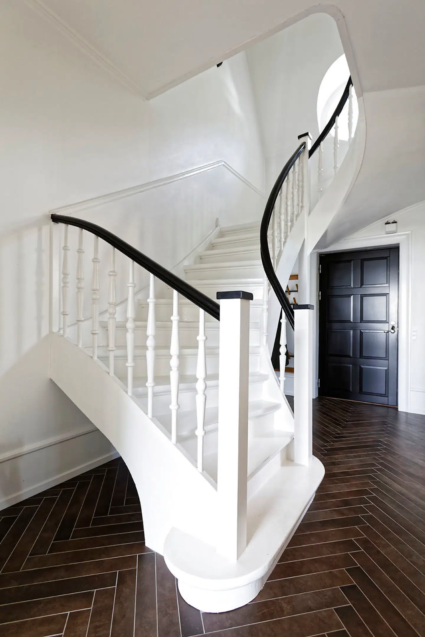 Den oprindelige trappe i hallen slynger sig skulpturelt op til overetagen. På gulvet er brune, italienske fliser, der går igen i badeværelset.