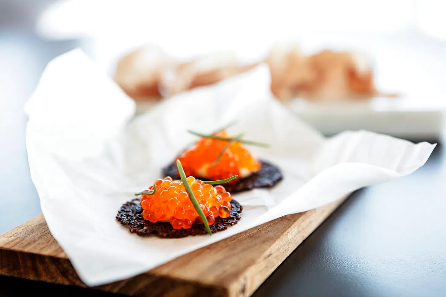 Første runde af snacks: En lille sprød rugbrødscrouton med røget creme, ørredrogn og i baggrunden fanøskinke.