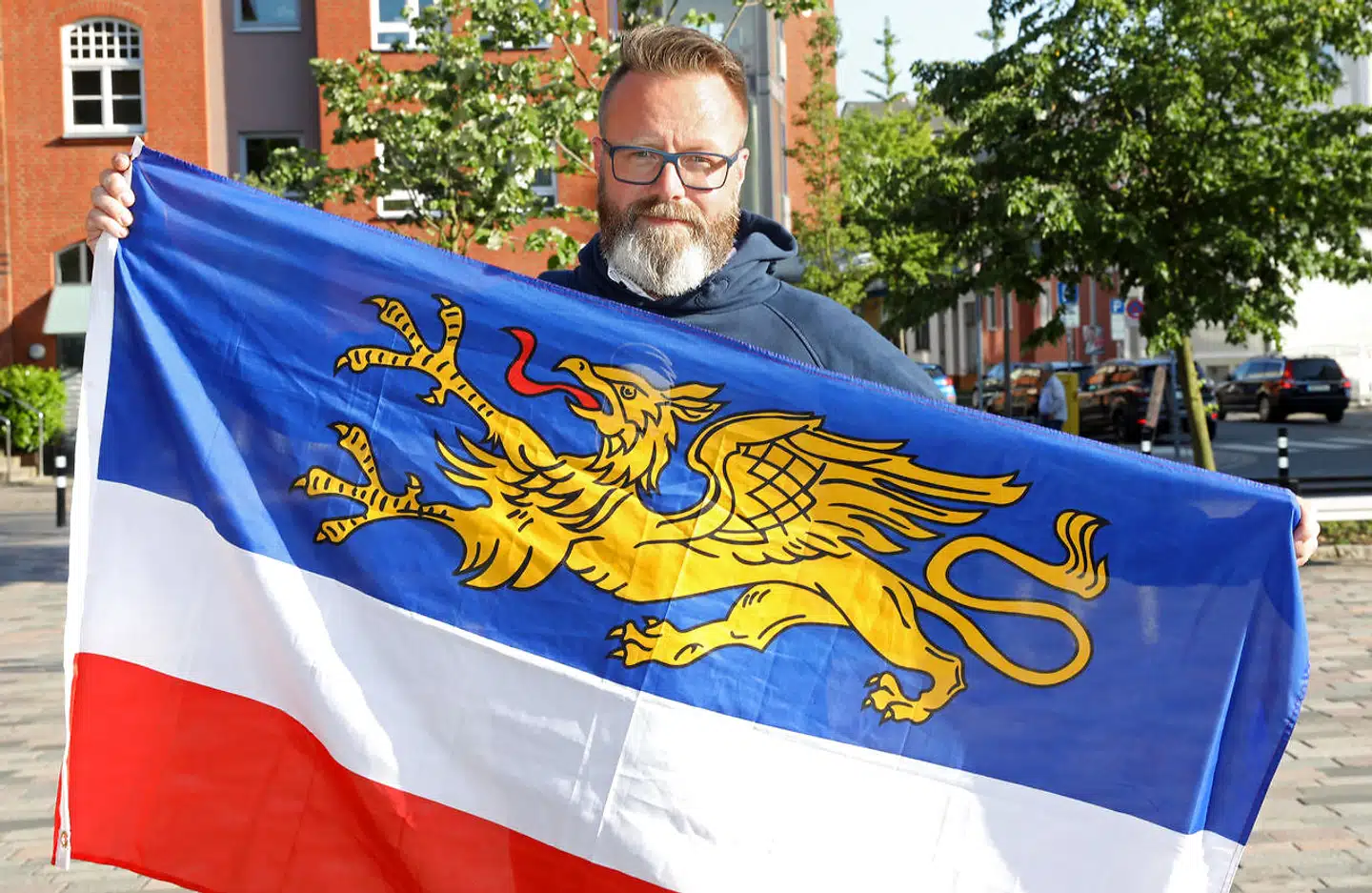 Danskeren Claus Ruhe Madsen, der her står med Rostocks flag, bliver den første udlænding, der kan sætte sig i overborgmesterstolen i en tysk storby. Ruhe Madsen stillede op som uafhængig i Rostock og blev støttet af kristendemokraterne, CDU, og det liberale FDP. I bystyret er der imidlertid et andet flertal Her skal Ruhe Madsen arbejde sammen med et flertal bestående af Die Linke, SPD og De Grønne.