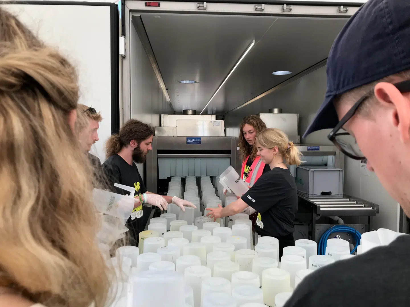 Først sættes de beskidte kander og krus op på båndet. De frivillige fortalte, at de hurtigt fandt en god rytme, hvor de sammen sørger for, at der ikke er »huller« i båndet, så de i stedet udnytter maskinens kapacitet til fulde.