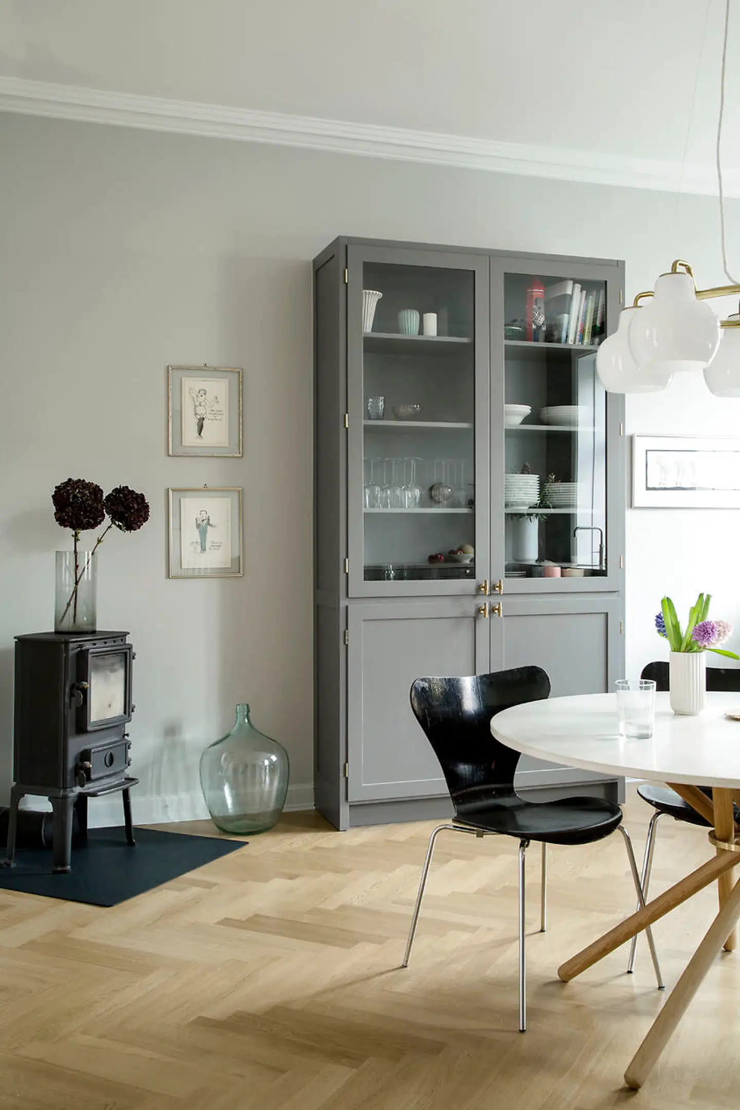 For at understrege stuestemningen i køkkenet har parret valgt at få bygget et vitrineskab magen til resten af køkkenet. Her står de ting, familien bruger mest, så det er lige ved hånden, og parret synes, det skaber hygge, at man ikke lukker alle ting inde bag låger. Den smukke lysekrone af Vilhelm Lauritzen binder rummet sammen og matcher med de runde linjer det runde spisebord fra Eberhart. Syver-stolene er fra Casper Brandis' forældres garage.