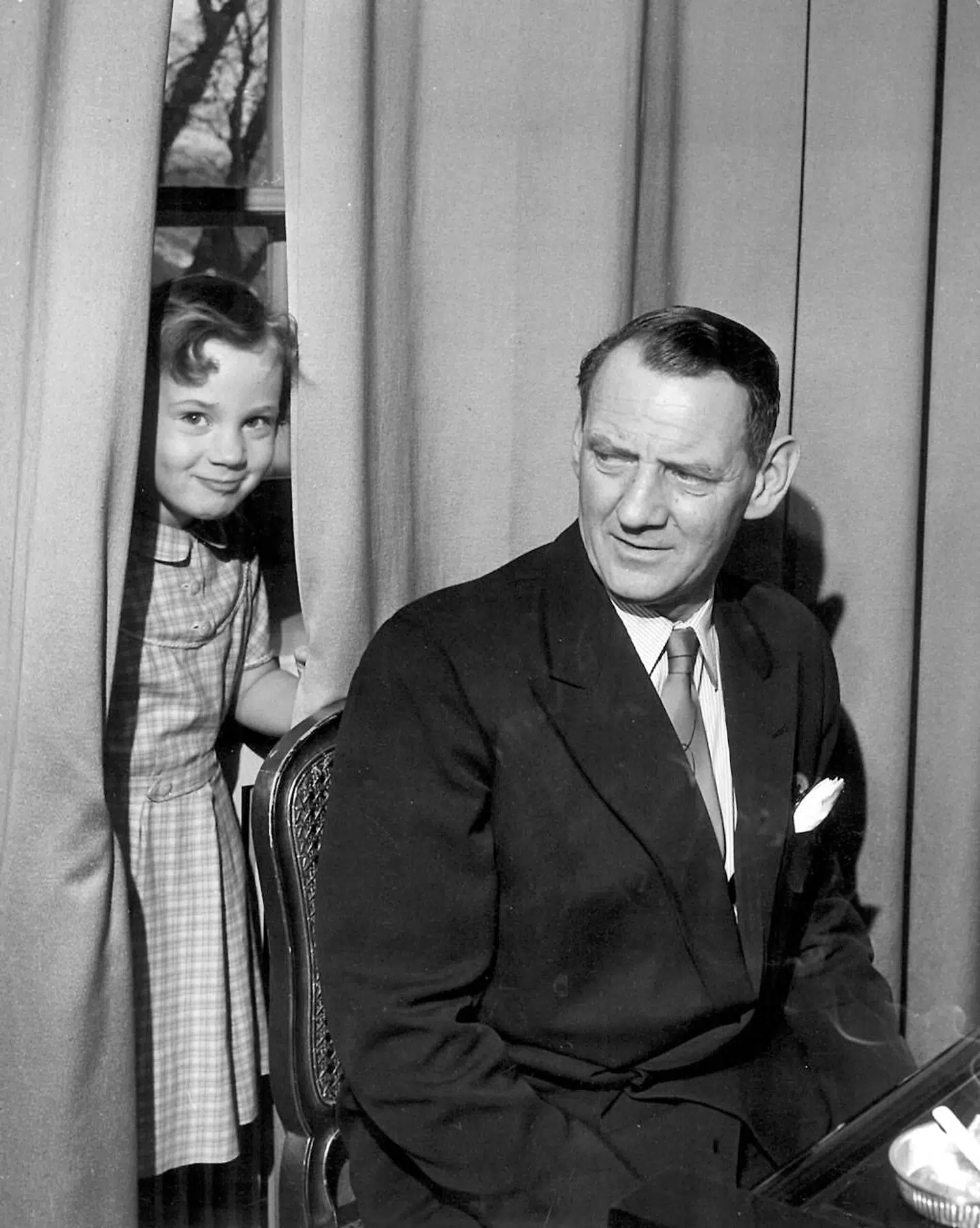 1951. Kong Frederik ved klaveret lader sig distrahere af den 8 årige prinsesse Benedikte, der skælmsk titter frem bag ham.