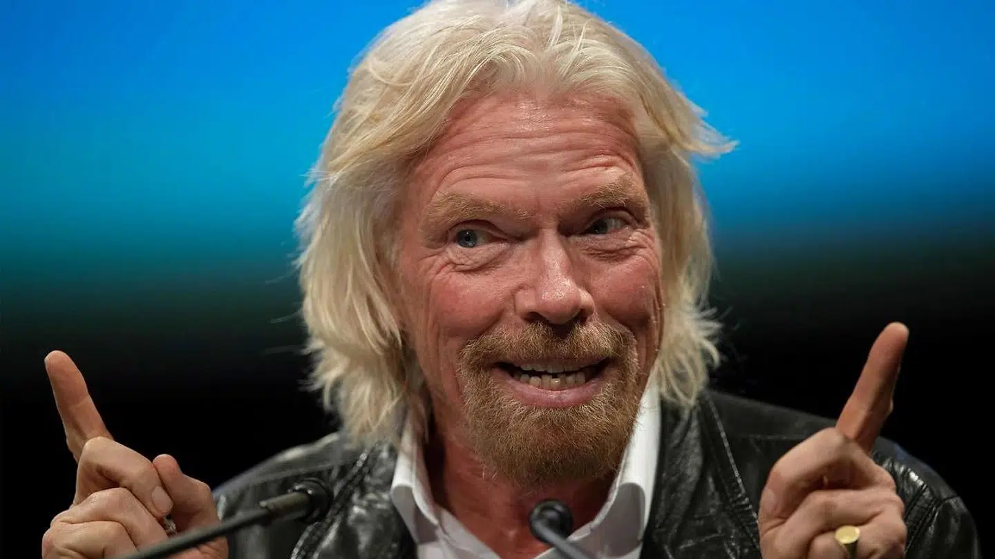 Richard Branson i sit es med stort smil og vinderfingrene i vejret, her under en tale på National Air and Space Museum i Washington i februar i år. Rummet optager ham meget – også i højere luftlag, end hans flyselskab kommer.