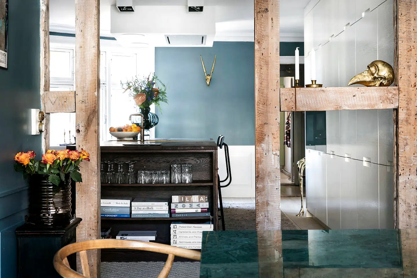 Fra det store samtalekøkken er der åbent ind til spisestuen, hvor den grønne vægfarve fanges af det grønne marmorspisebord. De høje skabe er også bygget af Handcrafted Interior, også i røget eg. Men parret valgte at få dem malet hvide på ydersiden, fordi det var for overvældende med alt det brune. På køkkenøen står en blå Balloon-vase fra Louise Roe, som også har lavet vasen til venstre.