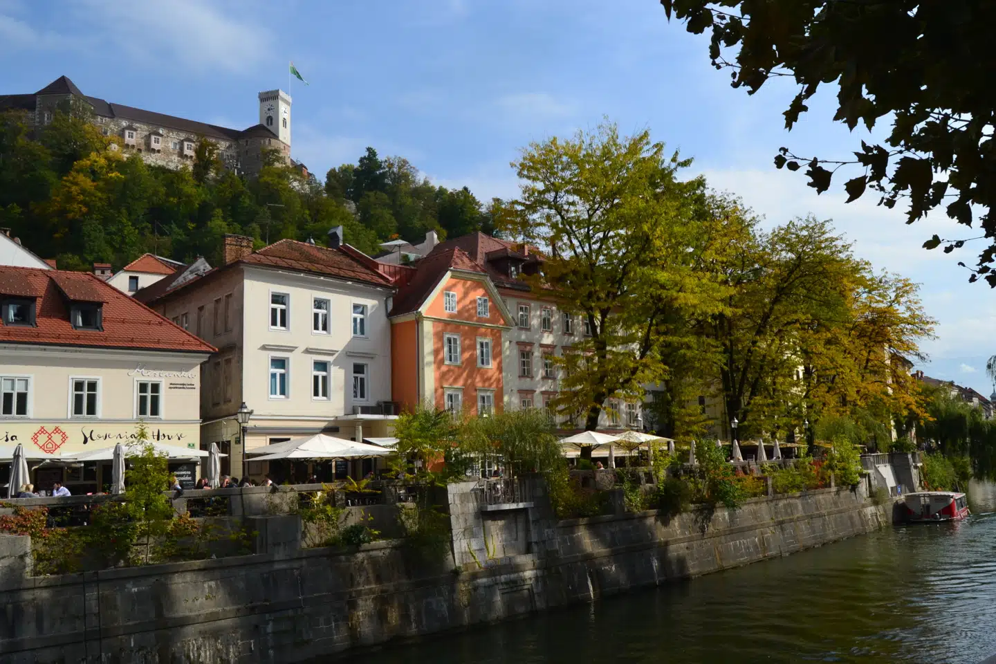 På en flodsejlads kommer man tæt på mange af byens smukke broer, facader og tårne. Over byen knejser Ljubljana Grad.