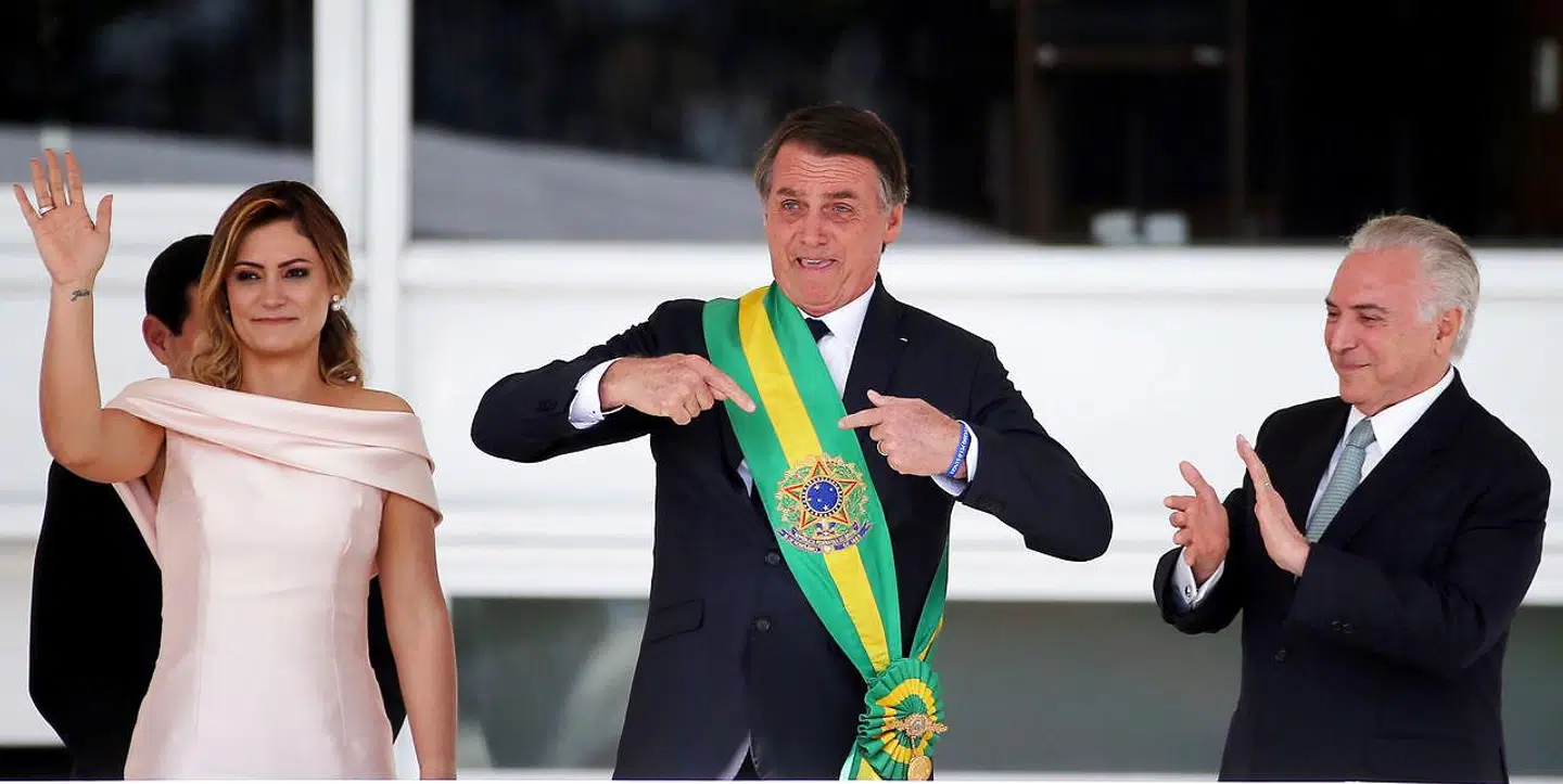 Brasiliens nye præsident, Jair Bolsonaro, modtager det præsidentielle skærf af sin forgænger, Michel Temer (t.h.), mens hans kone, Michelle Bolsonaro, vinker til de forsamlede tilhængere.