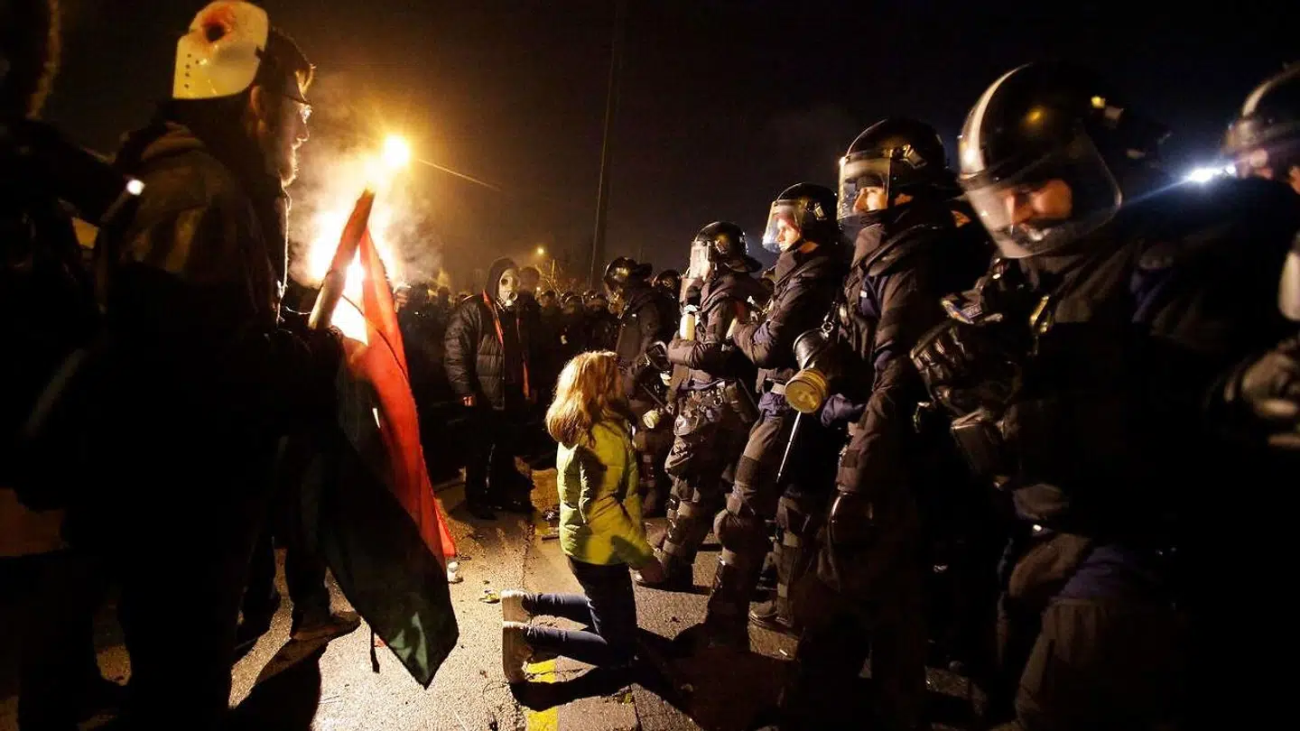 En demonstrant knæler foran en række politibetjente ved søndagens protester i Budapest. Flere end 10.000 demonstranter marcherede søndag mod det ungarske parlament og en statsejet TV-station for at protestere mod den ny »slavelov«. Politiet svarede igen med tåregas.