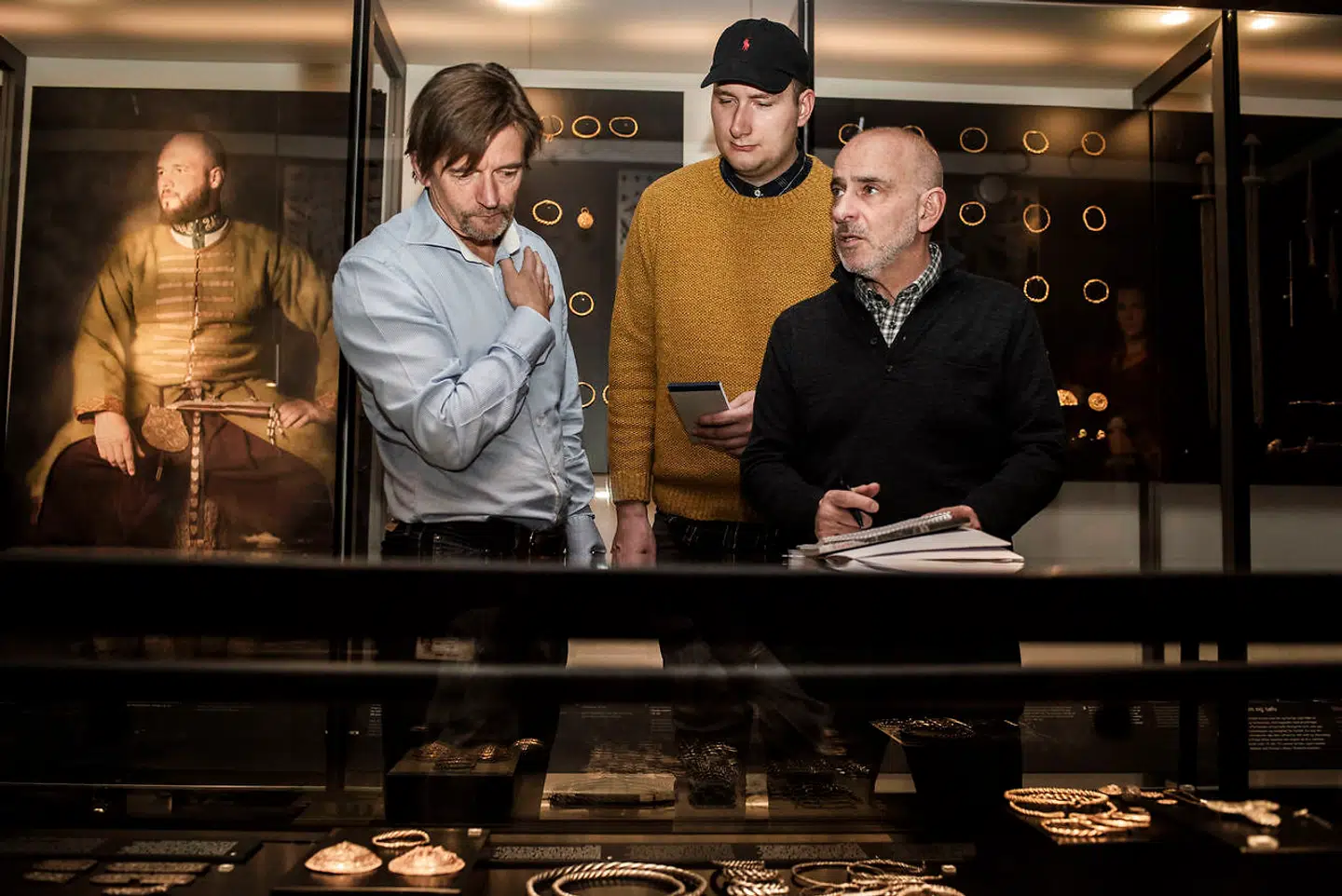 Bent Blüdnikow og Frederik Volstrup Kock får forklaret, hvor smykkerne i montren stammer fra.