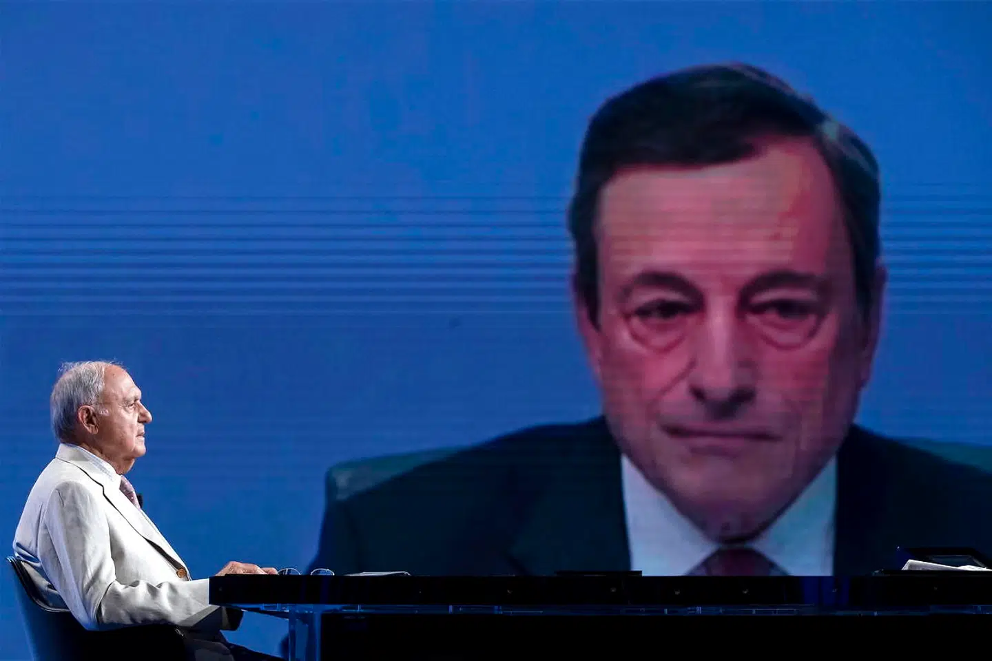 Europaminister Paolo Savona, der er erklæret euromodstander, deltager i et TV-program med et stort portræt af den italienske chef for den Europæiske Centralbank, Mario Draghi, som »bagtæppe«. Bankchefen opfordrede i weekenden såvel sine landsmænd som kollegerne i de europæiske institutioner til at skrue ned for retorikken.