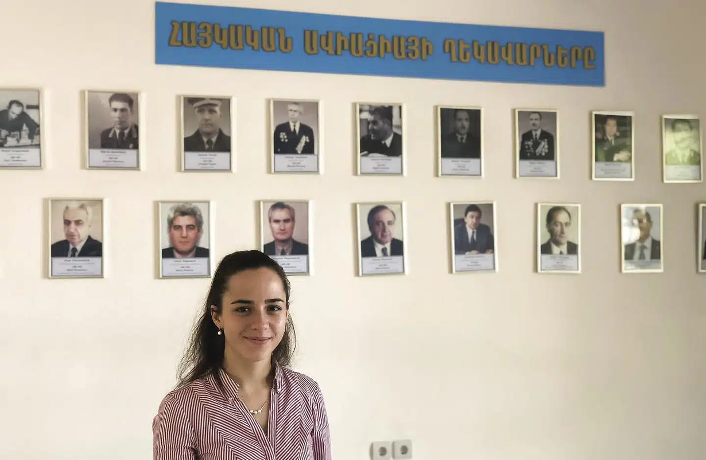 Tatevik Revazian er den yngste og den første kvindelige luftfartsvæsensdirektør i Armenien. Bag hende ses billeder af tidligere direktører.