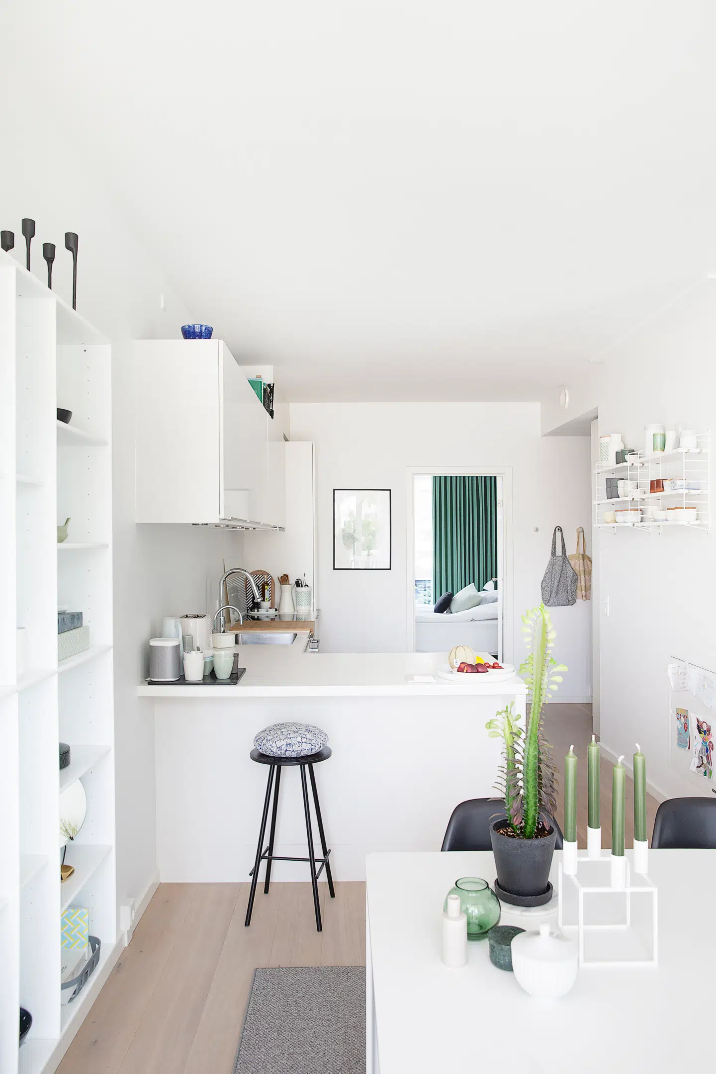 Kig igennem familiens lejlighed fra spisestuen til køkkenet og ind i parrets soveværelse. Farveskalaen er holdt diskret, men enkelte farver har fået lov til at komme indenfor som her den tidløse grønne i stearinlys, lysestager, planter og i det grønne velourgardin. Bonbonniere fra Lyngby Porcelæn, lysestager fra By Lassen og Holmegaard. Barstolen fra 8000C har fået en pude fra Daisy for ekstra komfort.
