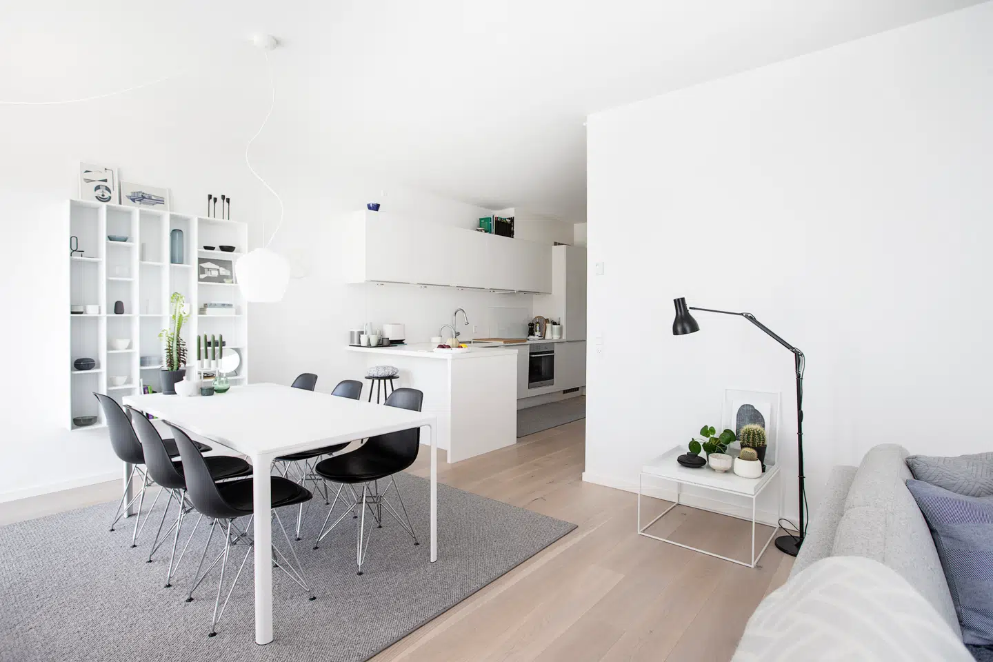 Den store spiseafdeling har plads til et lang, hvidt spisebord fra Fredericia Furniture med plads til 10 gæster på de seks Eames-stole, der er valgt i sort som kontrast. Gulvtæppet har Jesper Holkenberg fået specialfremstillet på mål, så det passer til rummet. Over en pendel fra AndTradition. Reolsystemet på væggen er fundet hos ABC-Reoler. Til højre er familiens køkken fra HTH placeret. Her er valgt hvide, diskrete elementer, og en stor køkkenø med plads til at spise lidt morgenmad.