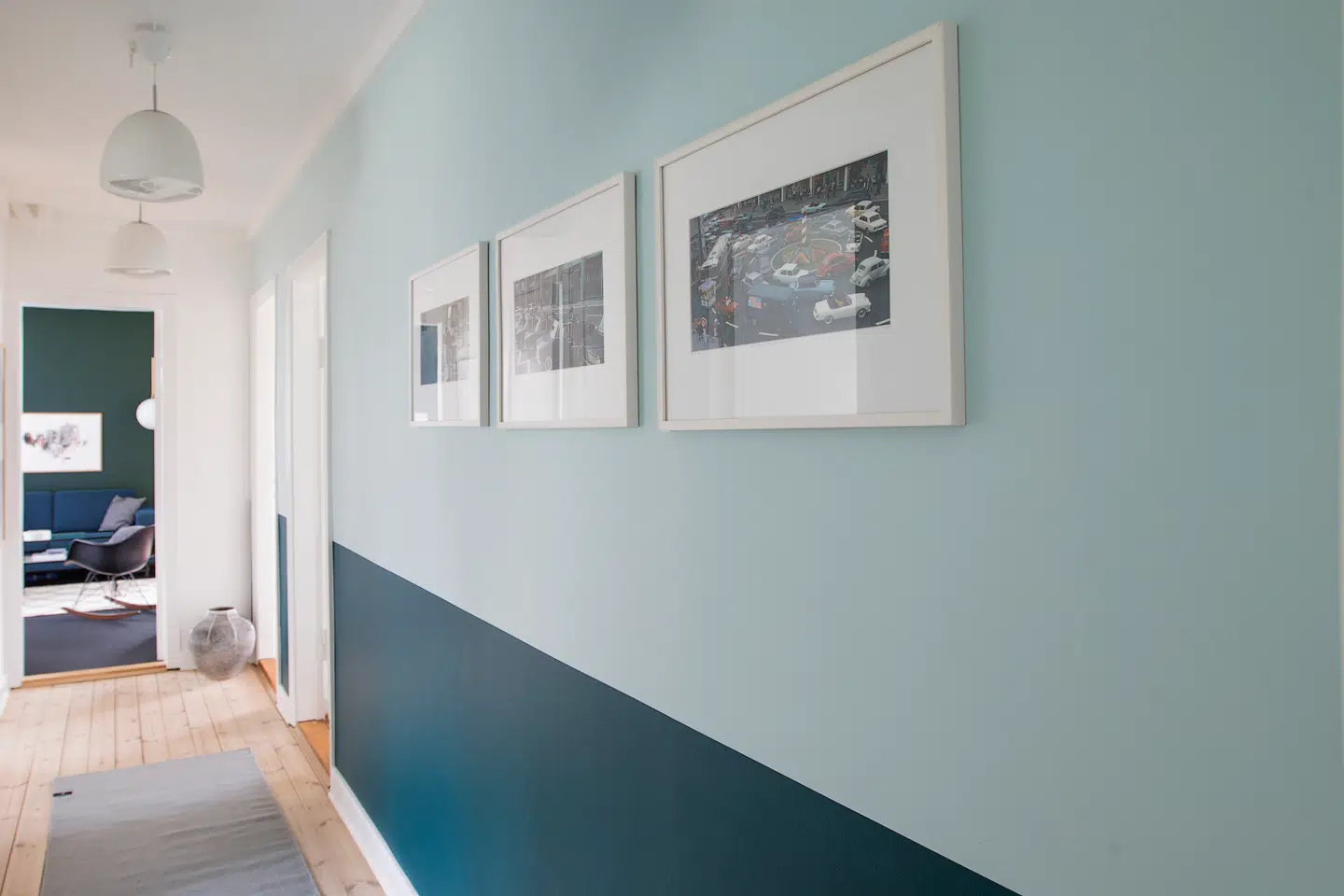 Parret har malet den ene væg i den lange fordelingsentré i to nuancer af grøn. Den øverste er en lys mint, mens den nederste er en mørkegrøn. Tricket skaber liv og farve i en lang gang, som parret ellers synes var lidt kedelig i hvid. Dertil har Nanna Brinkler hængt tre værker af Jacques Tati. De to pendler er vintage Holmegaard, og de er som huset fra 1950erne.