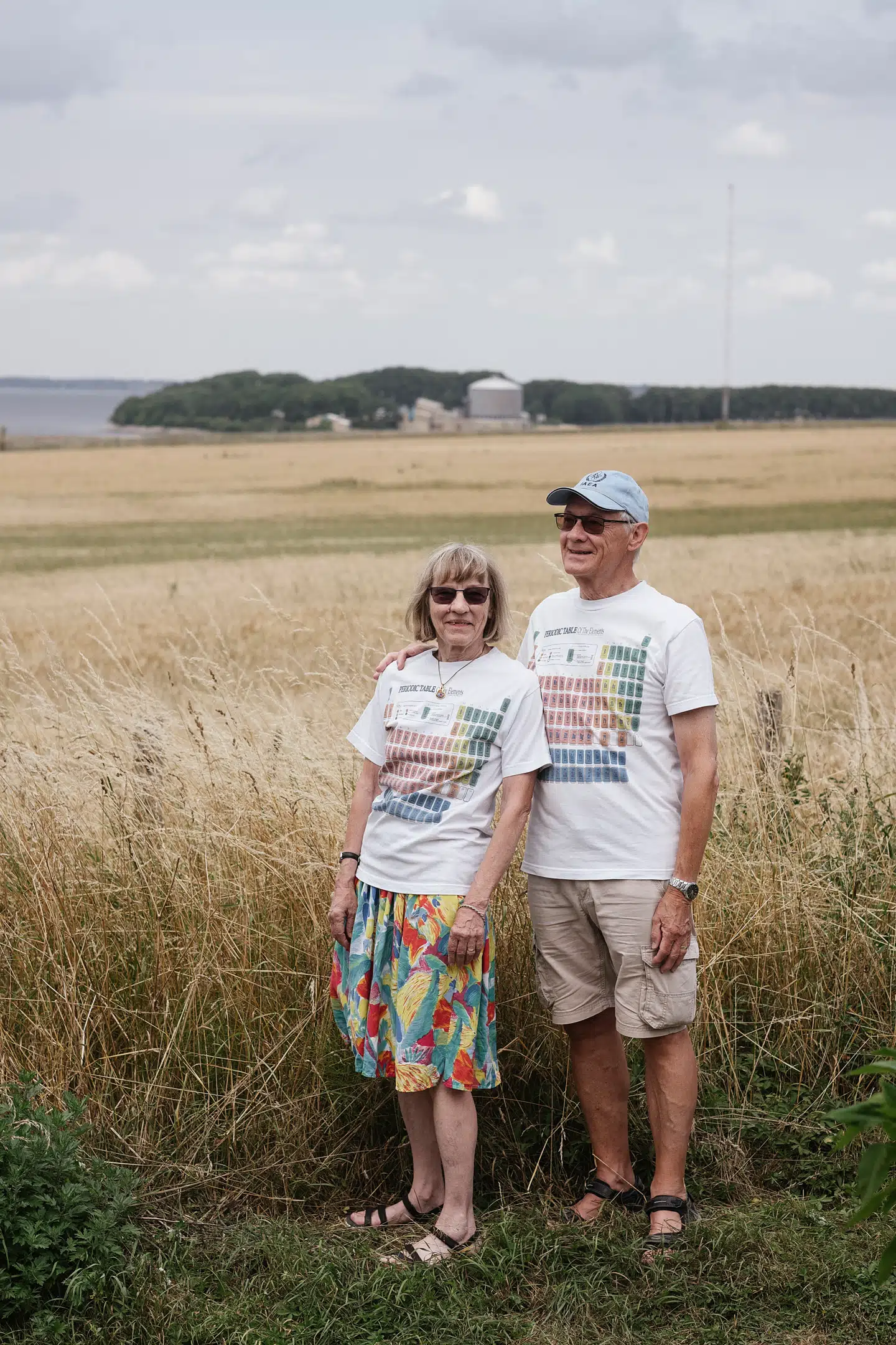»Det var med en vis ærefrygt at komme derind. Atomkraft var hjertebarnet.« Bente og Kurt Lauridsen, med det periodiske system på T-shirten og med Risø i baggrunden, hvor de har brugt hele deres arbejdsliv. De bor stadig i nærheden af værket. Foto: Asbjørn Sand