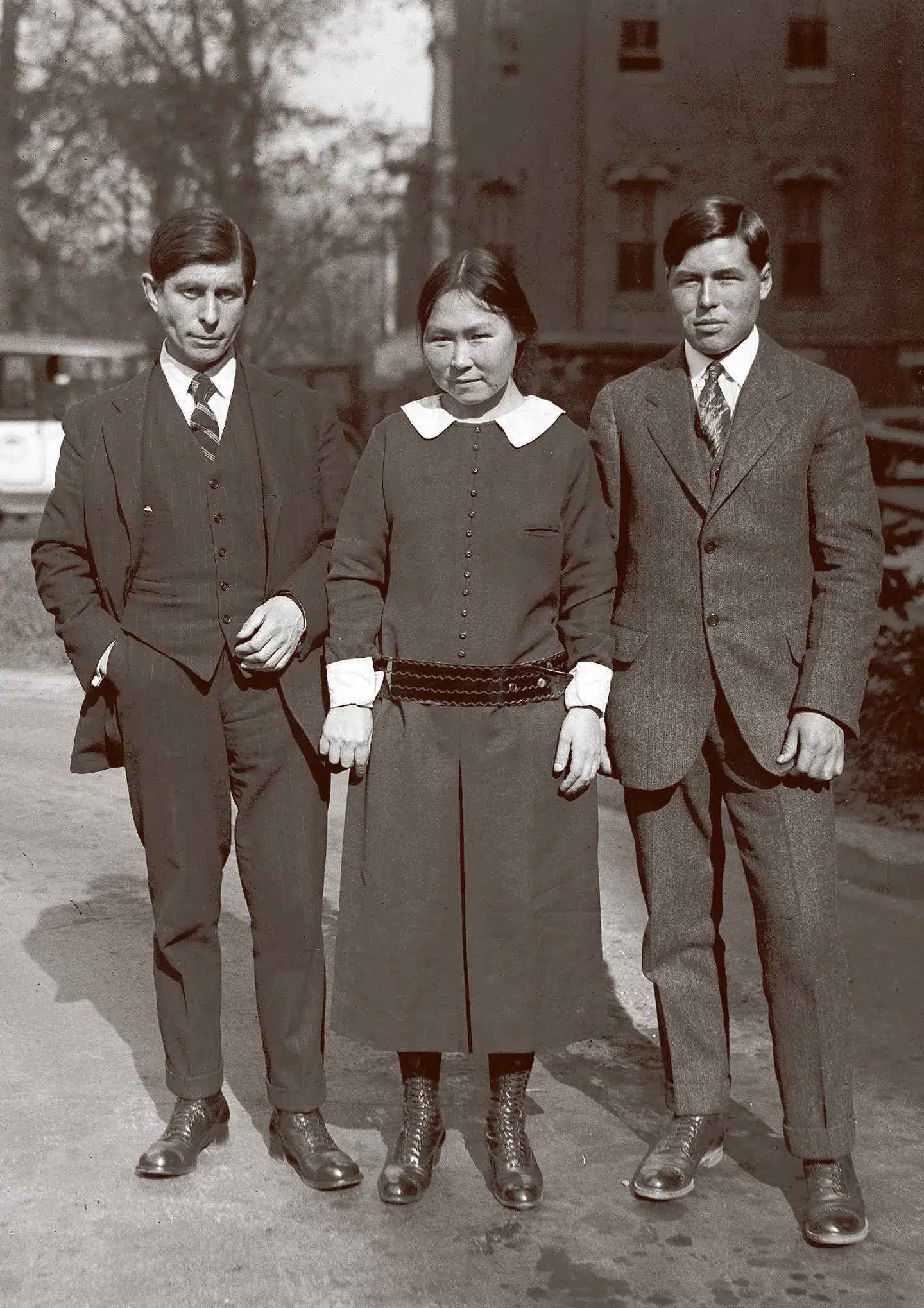 Døden på skyskraberen. Her endte Knud Rasmussens verdensberømte 5. Thule-ekspedition – i New York for enden af den skyskraber, hvor de tre rejsekammerater netop har været oppe og beskue »civilisationen«. I midten står i fin, moderne kjole Arnarulunguak (Det lille kvindemenneske), som mest havde undret sig over, hvor alle de mennesker dernede dog fik noget at spise fra. Hun og hendes fætter Miteq (Edderfuglen) til højre for hende var forudsætningen for, at de sidste 12.000 km af den tre år lange slæderejse over det amerikanske kontinents nordkyst blev fuldført – med livet i behold. Først ved Beringstrædet hørte den op. Det var hende, der reparerede deres udstyr og skindklæder eller syede helt nyt skindtøj, inklusive kamikker. Det var hende, der tilberedte maden, når der var fanget noget. Det var hende, der selv var en habil fanger og jæger. Og når de nærmede sig en fremmed stamme, var hun garantien for, at Knud ikke var på »kvinderov« og dermed på forhånd i betydelig livsfare. Hun døde kun 40 år gammel af tuberkulose. Det er ikke i Den store slæderejse, Knud Rasmussens »standardværk« om ekspeditionen, man finder dette højdepunkt beskrevet, men derimod på de sidste sider i Fra Grønland til Stillehavet. Der kommer lige akkurat et stille »ak« fra Arnarulunguak. Som Knud Rasmussen havde oplevet det så ofte før, når han på sine rejser talte med vildmarkens mænd og kvinder, om trængsler eller lykke, om fest eller hverdag, »altid var tonen stilfærdig og ægte. Og selv midt i virvar og kaos svigtede den ikke i Arnarulunguaks undrende udbrud«. Hun så de bittesmå mennesker dernede pile rundt i tusindvis imellem hinanden. Uden vildt! Og dog lever de og får deres mad, siger hun. Det er her, hun selv får et nyt – eller andet – liv og må sætte det forrige til. Hun dør den »død«, som Knud Ramussen tiltænkte hende og hendes folk det. Det var uundgåeligt. Deres oprindelighed måtte dø for, at de kunne leve videre i den herskende moderne verden. Men i Knud Rasmussens værker overlevede oprindeligheden – ikke som livsform, men som erindring, som ånd. Arkivfoto: Library of Congress