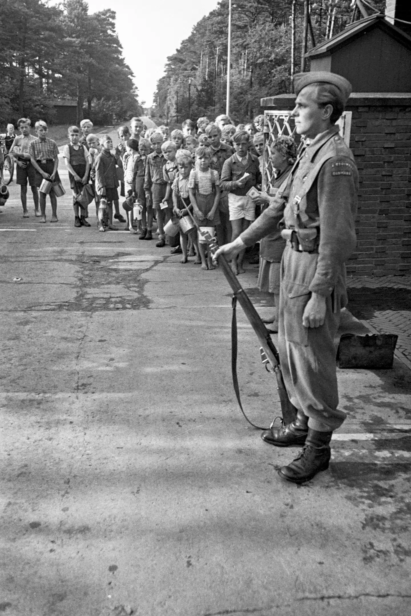 En dansk vagtpost foran en af Tysklandsbrigadens kaserner. Ude på vejen venter børn med spande på at få lov til at komme indenfor efter madrester. Foto fra bogen