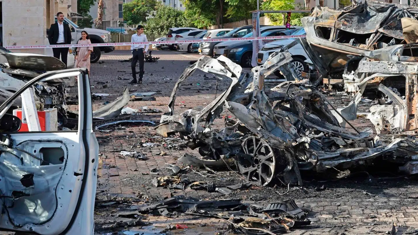 Beboere ser på vrag af ødelagte køretøjer i den israelske by Ashkelon efter et raketangreb fra Gazastriben.