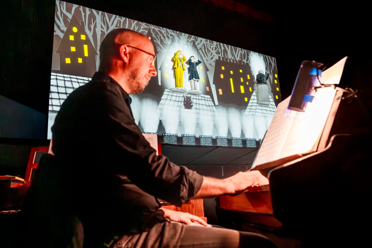 Robert Houssart spiller på klaverklokkespil i orkestergraven, med hovedpersonerne Papageno, Pamina og Monostatos hængende på scenen bag ved.