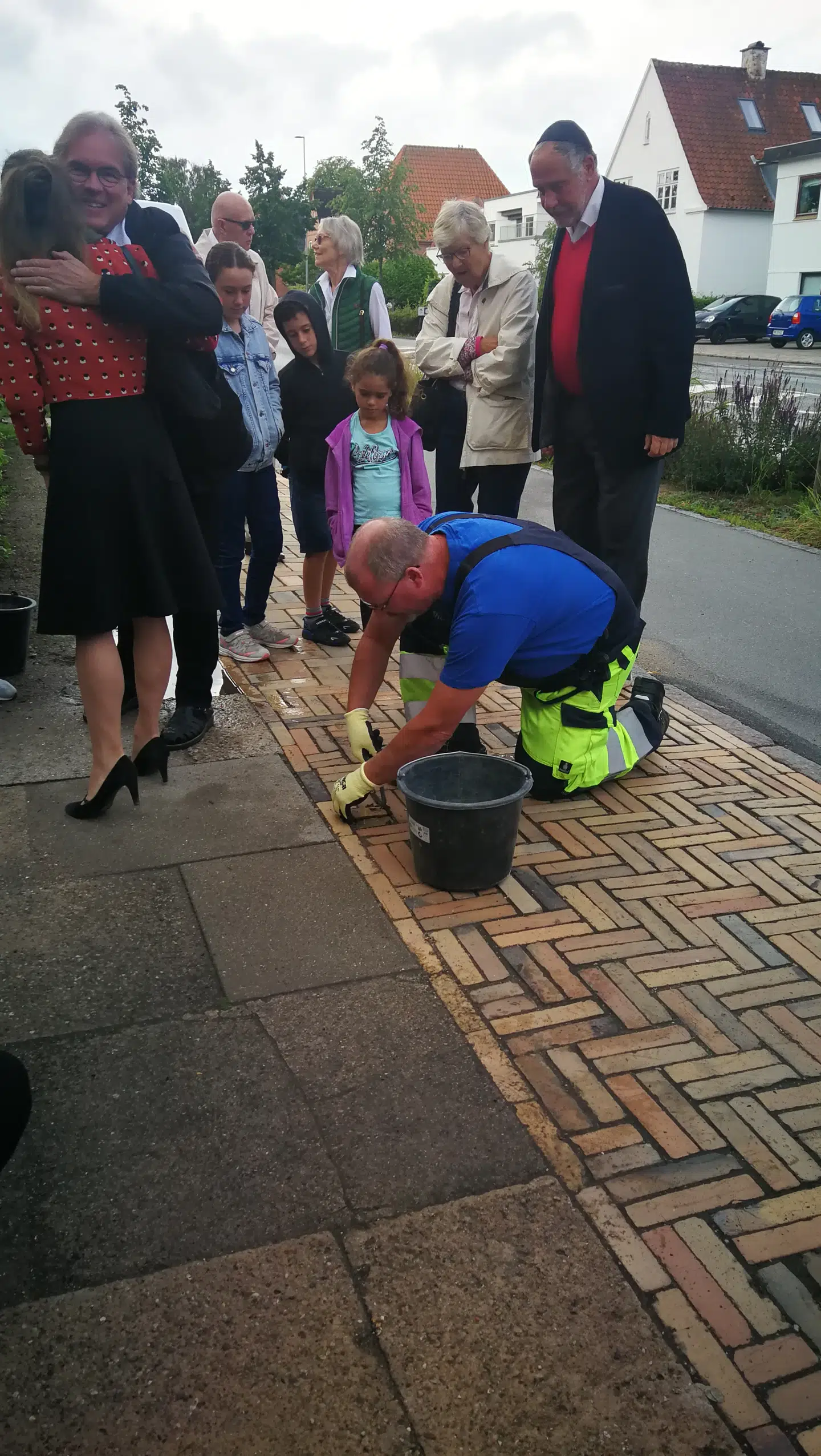 Som regel er kommunerne meget villige med at få lagt snublesten, men i Odense kommune gik det nær galt. Et politisk flertal i kommunen besluttede i første omgang at sige nej til snublesten af hensyn til husejerne - blev der argumenteret. Efter offentlig debat blev beslutningen ændret. Her ses stennedlæggelsen i år for Axel Metz, der døde i Theresienstadt. Til højre ses fhv. overrabbiner Bent Lexner og hans hustru Merete, der er født Metz og er en kusine til Axel Metz. Foto: Ira Hartogsohn.
