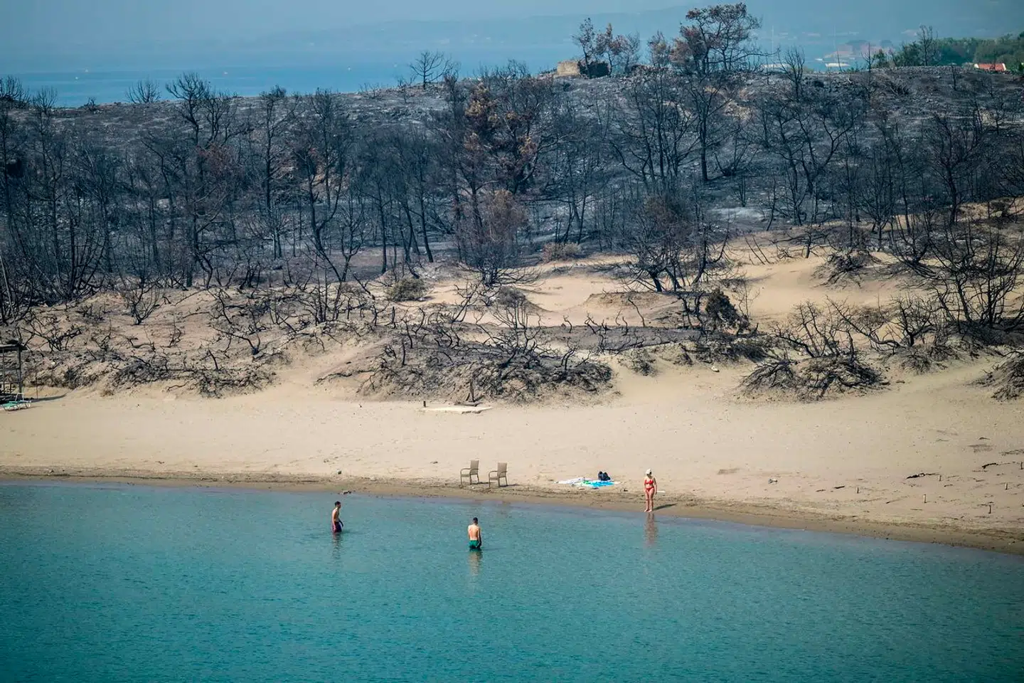 Kontrast: Her ses badende turister med de afbrændte skovområder i baggrunden på den populære græske ø Rhodos i sommer.